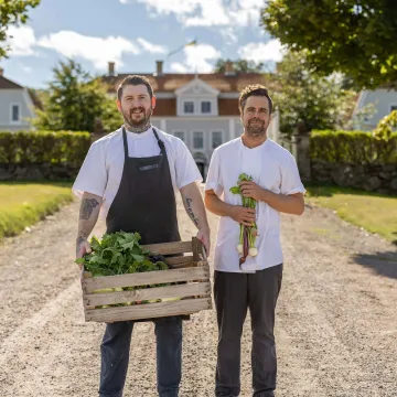 två kockar framför herrgårdsbyggnad