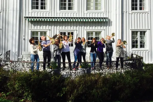 grupp människor som spelar blåsinstrument framför en vit herrgårdsbyggnad