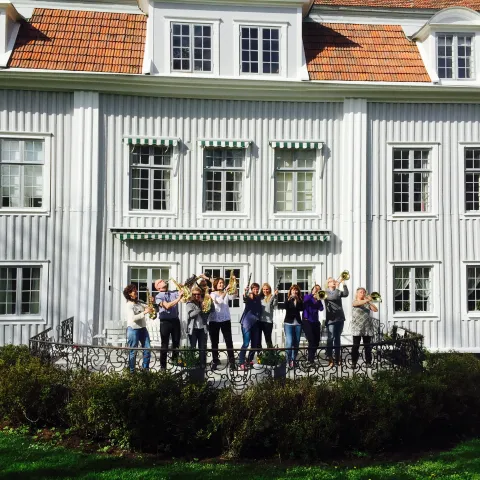 grupp människor som spelar blåsinstrument framför en vit herrgårdsbyggnad