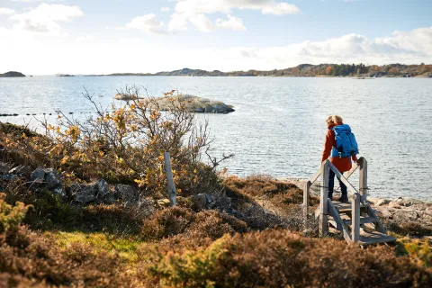 kvinna i röd jacka och blå ryggsäck vandrar vid havet